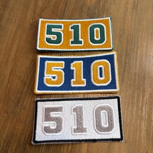 May include: Three rectangular embroidered patches featuring the number 510 in a collegiate font. The top patch is mustard yellow with dark green numbers, the middle is blue with yellow numbers, and the bottom is white with grey numbers.