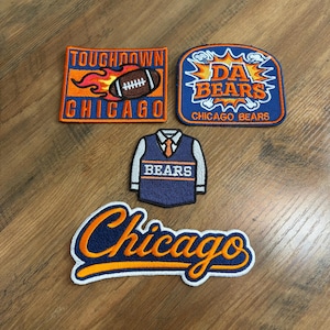 May include: Four embroidered patches featuring Chicago Bears themes. One rectangular patch says "TOUCHDOWN CHICAGO" with a flaming football. One shield-shaped patch says "DA BEARS CHICAGO BEARS". One jersey-shaped patch says "BEARS". One script patch says "Chicago".