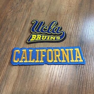 May include: Two embroidered patches featuring blue and yellow thread. The top patch displays the text Ucla BRUINS in a stylized script and block font. The bottom rectangular patch features the word CALIFORNIA in bold yellow block letters.