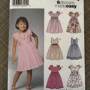 May include: Simplicity sewing pattern 5704 for girls' dresses. The pattern includes six dress designs, with sizes A 3,4,5,6,7,8. The cover features a girl wearing a pink gingham dress, and illustrations of the dress designs.