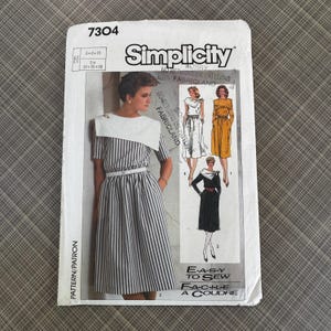May include: Simplicity sewing pattern 7304. The pattern features a woman in a striped dress with a white collar. The pattern also shows three other dress designs. The text "EASY TO SEW" and "FABRICLAND" are visible.