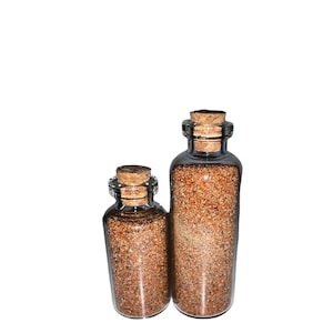 May include: Two glass bottles with cork stoppers filled with brown sand. The bottles are different sizes.