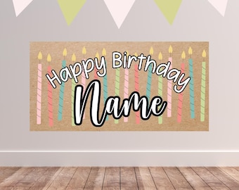 May include: A rectangular birthday banner with the words "Happy Birthday Name" in a whimsical font. The banner is decorated with colourful candles and a string of triangular flags.