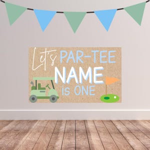 May include: A golf-themed birthday sign with the text "Let's PAR-TEE NAME is ONE." The sign features a green golf cart, an orange flag, and a green putting green. Blue and green pennant banners are strung across the top.