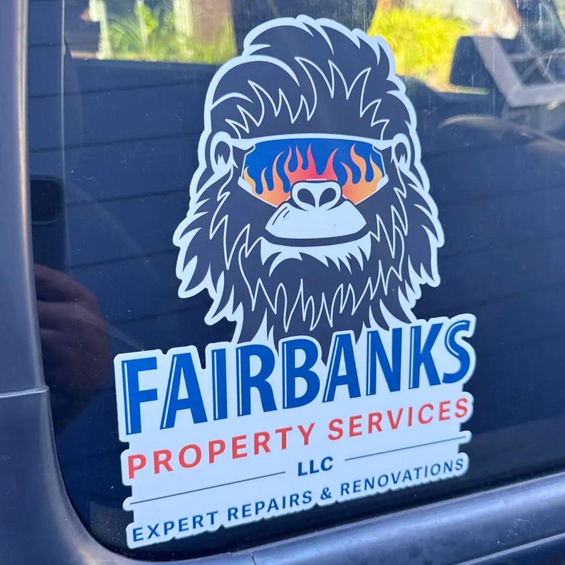May include: A sticker featuring a cartoon Bigfoot wearing sunglasses with a flame design. The sticker has the text "FAIRBANKS PROPERTY SERVICES" in blue and white, with "EXPERT REPAIRS & RENOVATIONS" below.