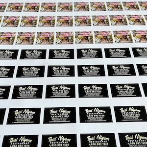 May include: Sheets of printed stickers featuring two distinct designs. One design showcases a mushroom image with text, while the other features the "Thai Niyom Restaurant" logo, address, and contact information in white on a black background.