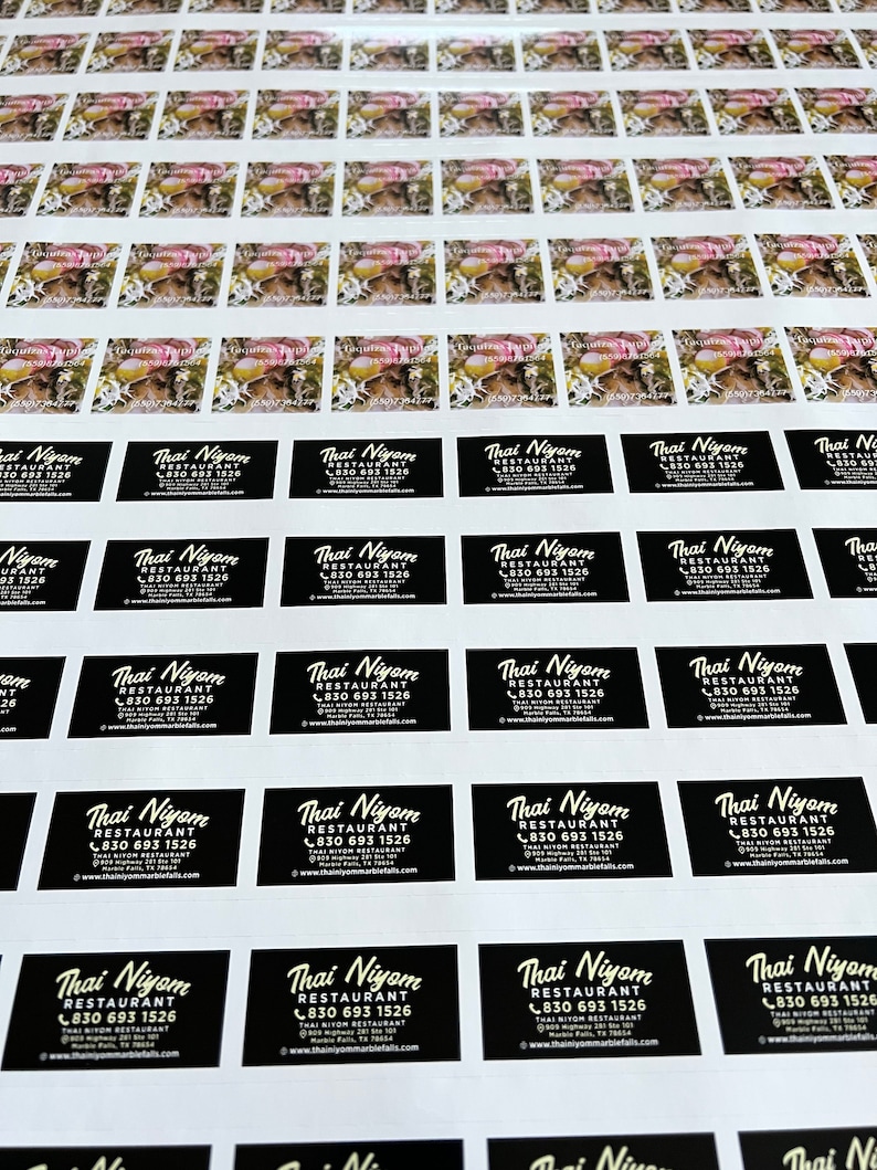 May include: Sheets of printed stickers featuring two distinct designs. One design showcases a mushroom image with text, while the other features the "Thai Niyom Restaurant" logo, address, and contact information in white on a black background.