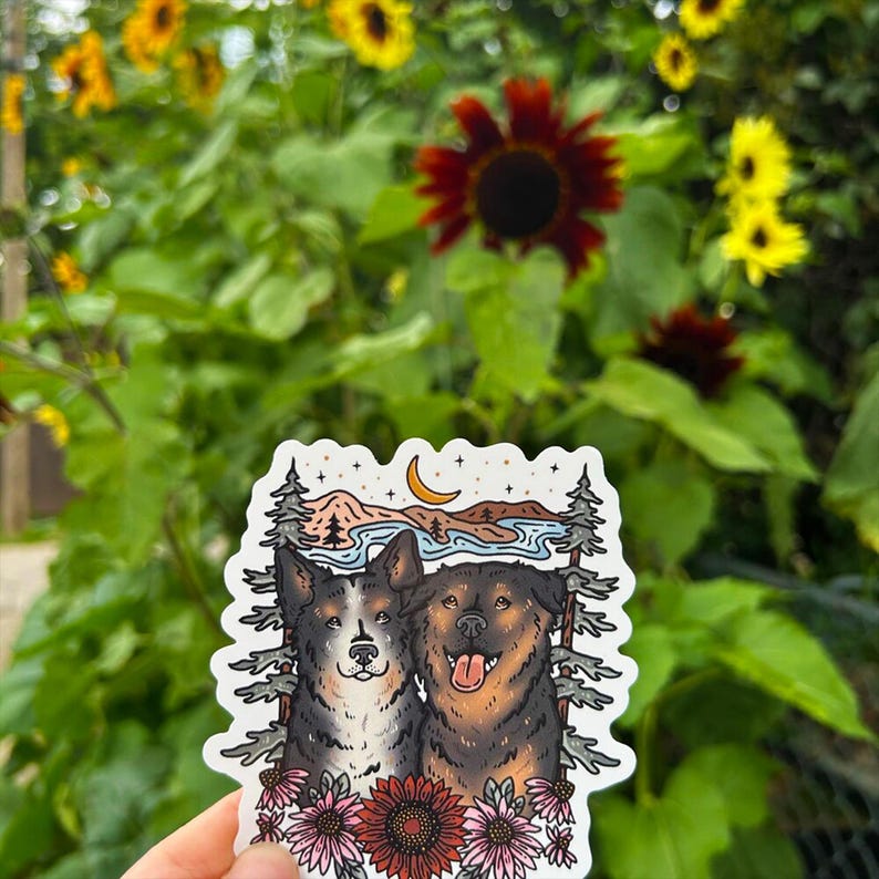 May include: A die-cut sticker featuring an illustration of two dogs, one black and white and one brown and black, framed by pine trees, mountains, a crescent moon, and stars, with a cluster of sunflowers at the bottom of the design.