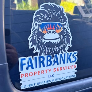 May include: A vinyl decal sticker featuring a dark gray, shaggy-haired creature wearing sunglasses with orange and blue flames. Below the graphic, the text reads FAIRBANKS PROPERTY SERVICES LLC, followed by the words EXPERT REPAIRS & RENOVATIONS.
