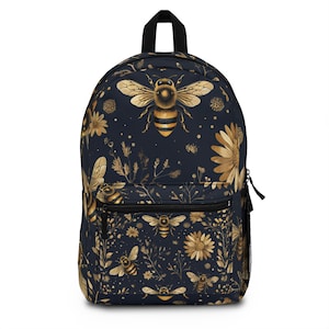 May include: A navy blue backpack with a gold bee and floral pattern. The backpack features a front zippered pocket, a black handle, and a mesh side pocket. The design includes detailed illustrations of bees, flowers, and foliage.