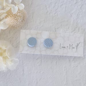 May include: A pair of light blue round stud earrings on a white card with the text "Lima + Mae".
