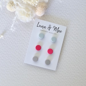 May include: A set of six stud earrings on a white card. The earrings are in three colors: light gray, dark gray, and pink. The card has the text "Luna & Mae Handmade Jewellery".