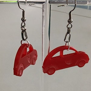 Puede incluir: Un par de pendientes rojos en forma de coche con ganchos plateados. Los pendientes están hechos de un material liso y brillante.