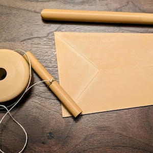 May include: A tan-colored wooden toy, likely a yo-yo, with a spool-like shape and a string, alongside a tan envelope and a wooden dowel. The items are arranged on a dark brown wooden surface.