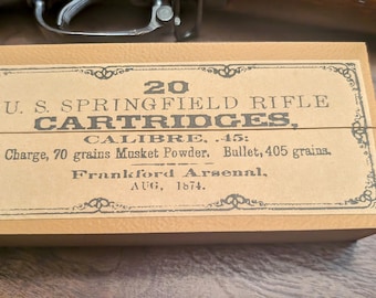 May include: A rectangular cardboard box with a label that reads "20 U.S. SPRINGFIELD RIFLE CARTRIDGES." The label also includes "CALIBRE .45" and other details. The box is tan with a decorative border and is from Frankford Arsenal, AUG, 1874.