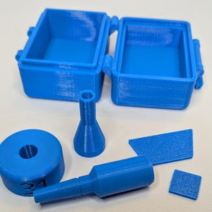 May include: A set of blue 3D printed parts, including a small box with a lid, a round piece with the number 31 on it, and three different shaped pieces.