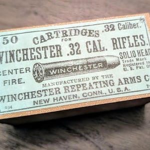 May include: A vintage box of Winchester .32 Caliber rifle cartridges. The box is light blue with gold trim and features text including "50 Cartridges", "Winchester", and "Solid Head". The box also includes an illustration of a bullet.