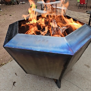May include: A large, octagonal fire pit made of metal with a blue-tinted finish. The fire pit has a wide opening and is filled with burning wood and flames.