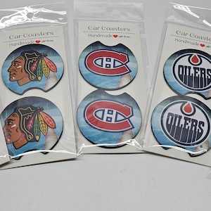 May include: Set of six handmade car coasters featuring various NHL team logos. The coasters are round and have a blue and white background with the team logo in the center. The logos include the Washington Capitals, Chicago Blackhawks, Montreal Canadiens, Edmonton Oilers, and Buffalo Sabres.