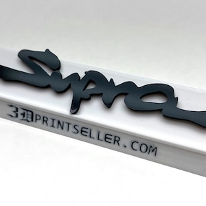 May include: A black "Supra" logo sits atop a white rectangular base. The logo is in a stylized font. The base has the text "3DPRINTSSELLER.COM" printed on the front. The background is white.