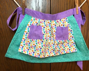 Jelly Beans hop allover the skirt of this pleated children's half apron. Matching bright colors for waistbands and underskirts finish it.