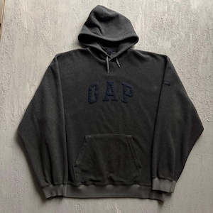 May include: A dark charcoal gray fleece hoodie featuring a hood with matching drawstrings, long sleeves with ribbed cuffs, and a large front kangaroo pocket. The word GAP is embroidered in a dark navy blue thread across the center chest area.