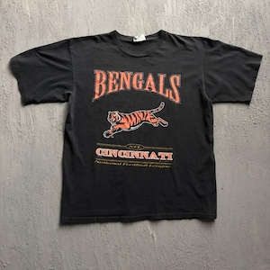 May include: A black short-sleeve t-shirt featuring a graphic of a leaping orange and black tiger. The text reads BENGALS in large orange letters, with CINCINNATI, NFL, and National Football League printed below the tiger in orange and white.