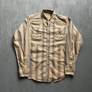May include: A long-sleeve button-down shirt featuring a tan and grey vertical striped pattern. The shirt includes two chest pockets with pointed flaps, a pointed collar, and silver-toned snap buttons down the front placket and on the cuffs.
