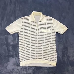 May include: A short-sleeved polo shirt in off-white featuring a repeating pattern of small, horizontal dark brown rectangular dashes across the front. The shirt includes a pointed collar, a V-neck opening, and a single small chest pocket on the left side.