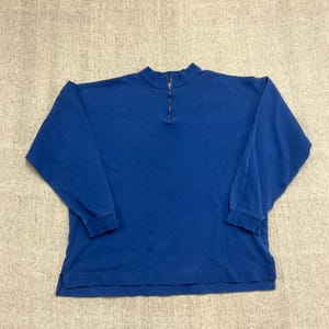 Peut inclure: Un sweat-shirt à manches longues bleu roi uni doté d'un col montant et d'une fermeture éclair métallique argentée d'un quart de longueur au centre. Le vêtement présente des manches longues à poignets côtelés et un ourlet droit avec fentes.