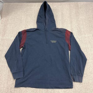 May include: Navy blue hooded sweatshirt with maroon shoulder accents. The sweatshirt has a drawstring hood and long sleeves. The text "Abercrombie 1892" is printed on the chest. A casual top suitable for everyday wear.
