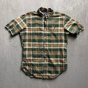 May include: A short-sleeved button-down shirt featuring a plaid pattern in shades of forest green, white, and mustard yellow. The shirt has a button-down collar, a front button placket, and a small embroidered logo on the left chest area.
