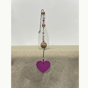 May include: A glass bottle with a pink and brown beaded string hanging from it. The string ends with a large purple heart.