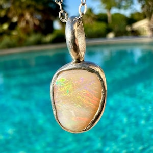 May include: A silver pendant featuring a white opal gemstone. The opal displays iridescent flashes of colour.