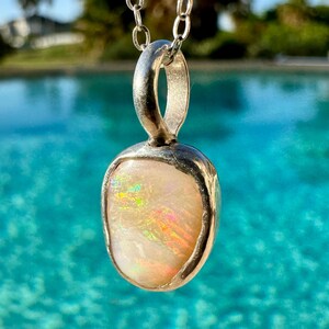 May include: A silver pendant featuring a white opal gemstone. The opal displays iridescent rainbow colours.