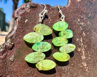 May include: A pair of silver dangle earrings with multiple green oval-shaped beads. The beads are translucent and have a light green color.