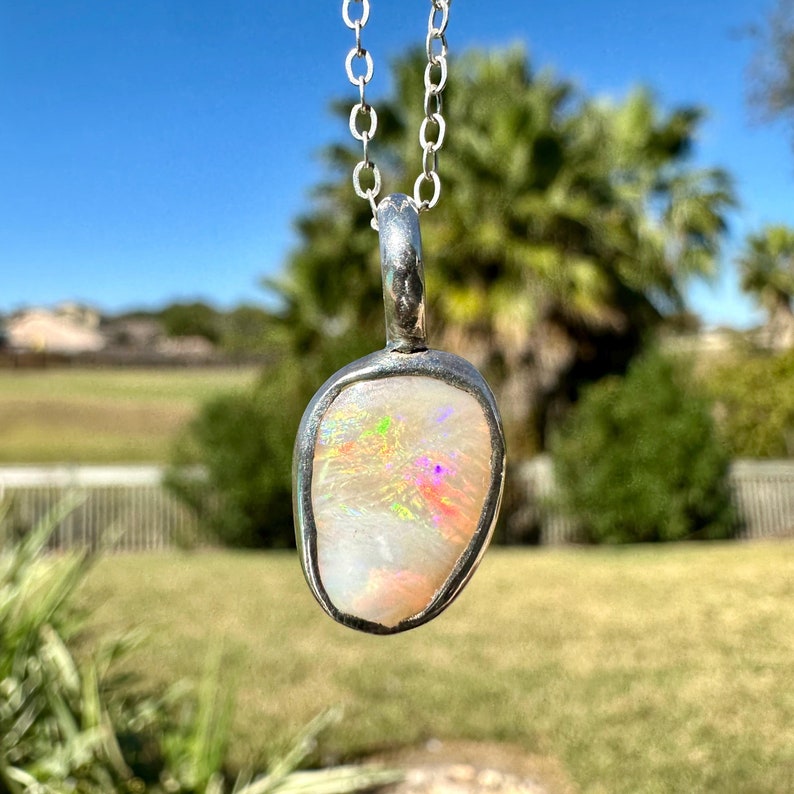 May include: A silver chain necklace with a pendant featuring a white opal stone with iridescent rainbow colours.