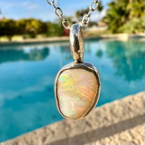 May include: A silver pendant necklace featuring a white opal gemstone. The opal displays iridescent rainbow colours.