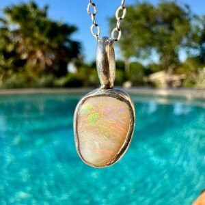 May include: A silver chain necklace with a pendant featuring a white opal gemstone set in a silver bezel. The opal has a rainbow iridescent sheen.