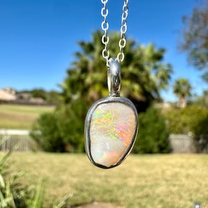 May include: A silver chain necklace with a pendant featuring a white opal stone with iridescent rainbow flashes. The pendant is set in a silver bezel.