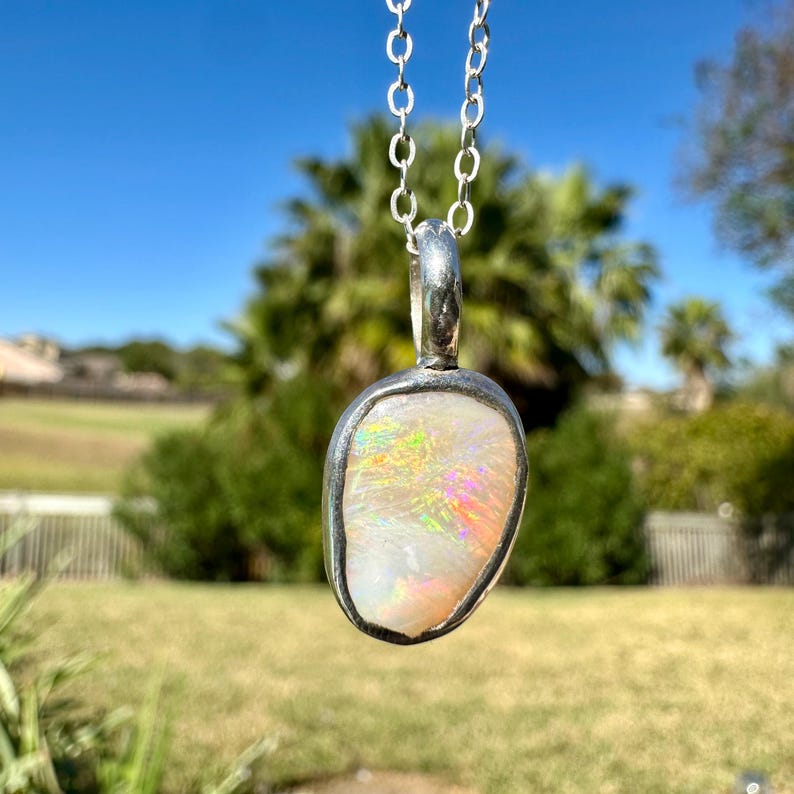 May include: A silver chain necklace with a pendant featuring a white opal stone with iridescent rainbow flashes. The pendant is set in a silver bezel.