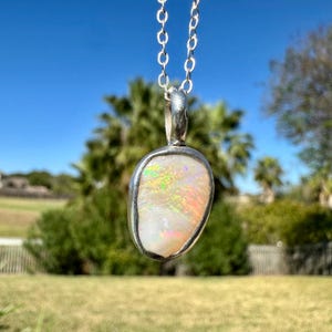 May include: A silver chain necklace with a pendant featuring a white opal stone with iridescent rainbow colours.