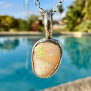 May include: A silver pendant necklace featuring a white opal stone. The opal displays a rainbow iridescent sheen.