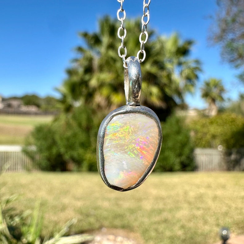 May include: A silver chain necklace with a pendant featuring a white opal stone set in a silver bezel. The opal has iridescent rainbow colours.