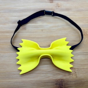 Puede incluir: Una pajarita amarilla con forma de fideo de pasta, con una correa negra ajustable.