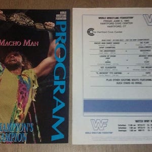 May include: A vintage wrestling program and event flyer. The program cover features "Macho Man" Randy Savage holding a championship belt. The flyer lists the event details, including the date, location, and match lineup.