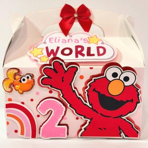 May include: A decorated party favor box featuring Elmo from Sesame Street. The box is pink and white with a red bow, the number 2, and the words "Eliana's World". A cartoon goldfish and rainbow are also featured.