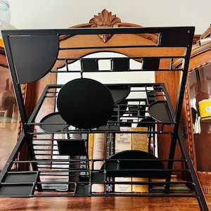 May include: A black metal book stand featuring a geometric design with various circular and rectangular cutouts. The frame is constructed from thin, interconnected metal bars, providing a stable structure for displaying books in an upright position.