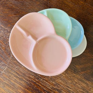 May include: Three ceramic paint palettes in pink, light blue, and green. The palettes are nested inside each other, with the pink palette on top.