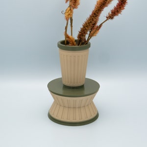 May include: A beige and green ceramic vase with a fluted design. The vase is filled with dried flowers.